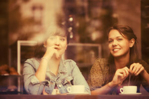 Two women sitting in a window of a coffee shop enjoying drinks